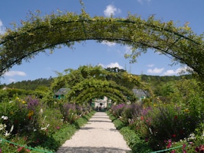 A lush garden pathway lined with vibrant flowers and trimmed bushes under a sunny sky.