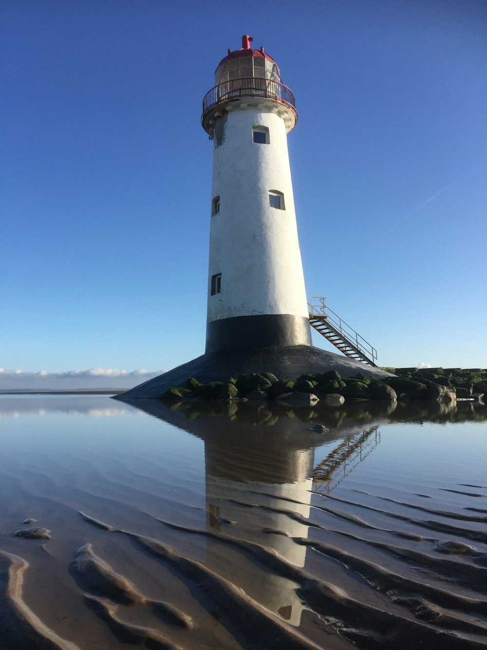 weißer und schwarzer Leuchtturm in der Nähe von Gewässern tagsüber