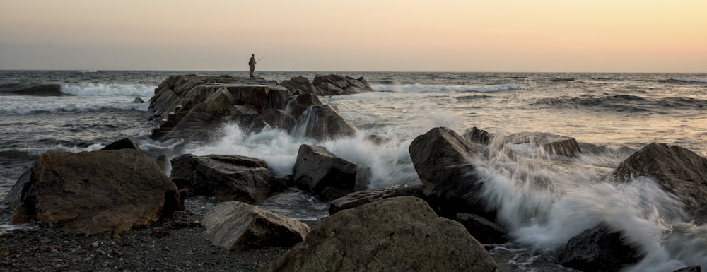 person standing on rock formation near sea waves during daytime