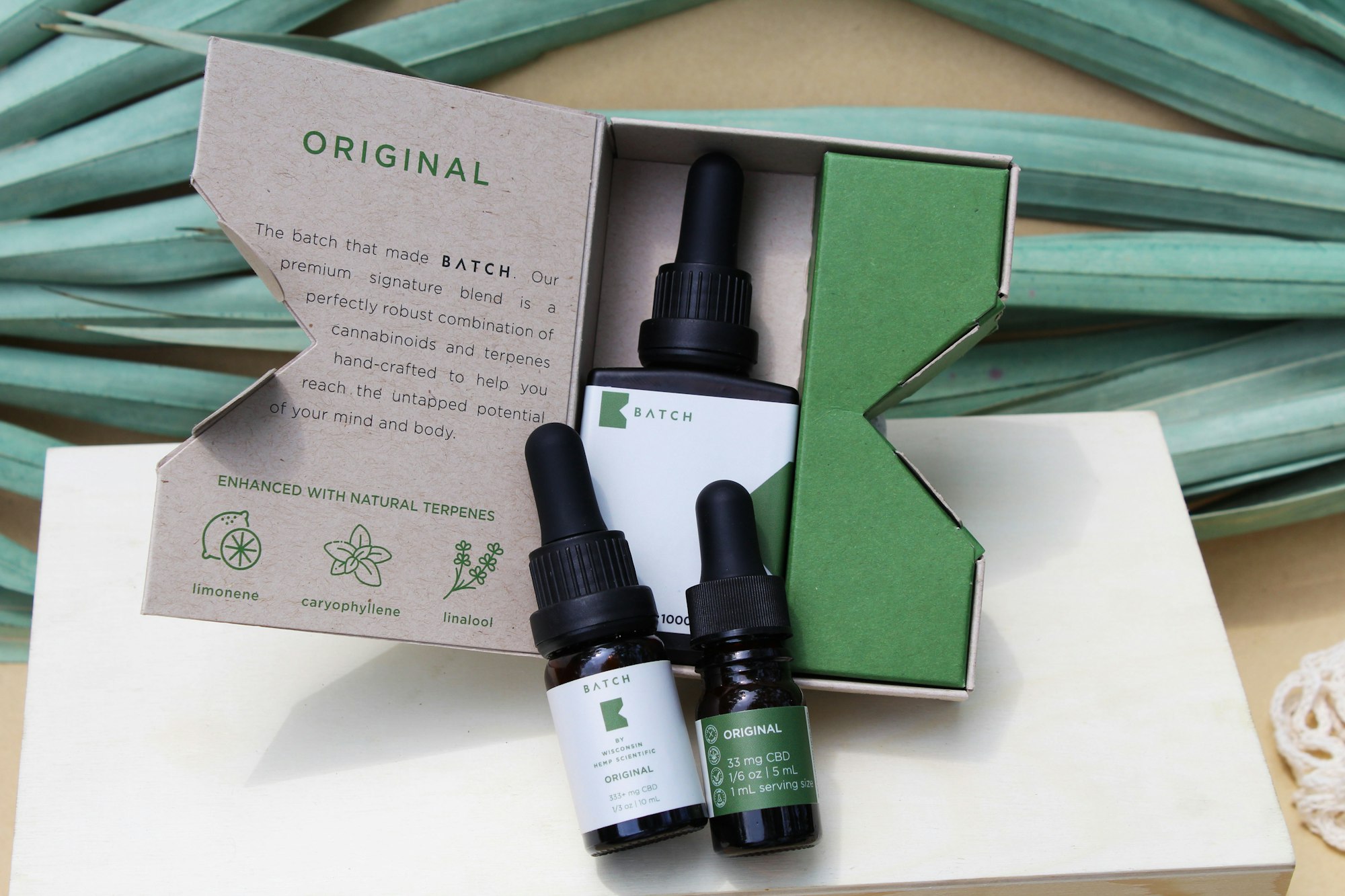Original CBD oil tinctures displayed on wooden box with palm branches and aesthetically pleasing background