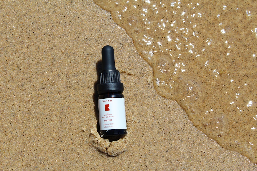 Miniature CBD oil tincture in the sand at beach with wave splashing