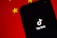 A smartphone displaying the TikTok logo on its screen, set against a background with the colors and patterns resembling the Chinese flag, predominantly red with yellow stars.