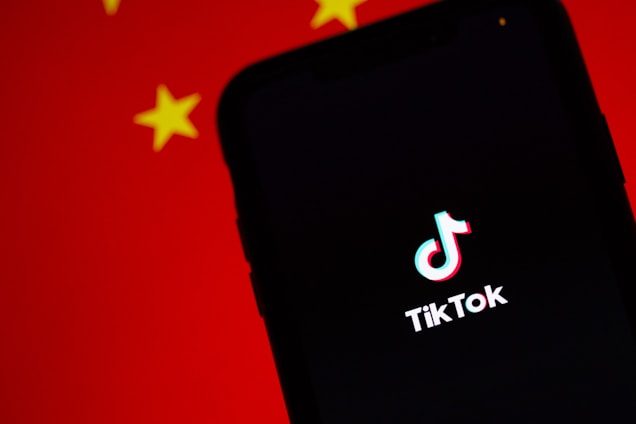 A smartphone displaying the TikTok logo on its screen, set against a background with the colors and patterns resembling the Chinese flag, predominantly red with yellow stars.