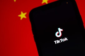 A smartphone displaying the TikTok logo on its screen, set against a background with the colors and patterns resembling the Chinese flag, predominantly red with yellow stars.