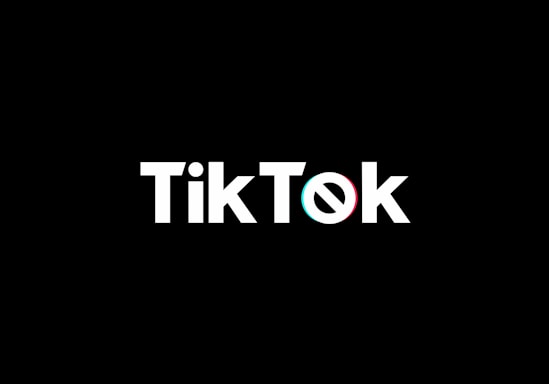 A minimalist logo featuring the word TikTok in a bold, white font centered on a black background. The 'o' in TikTok is stylized with a design resembling a musical note, incorporating subtle blue and red hues.