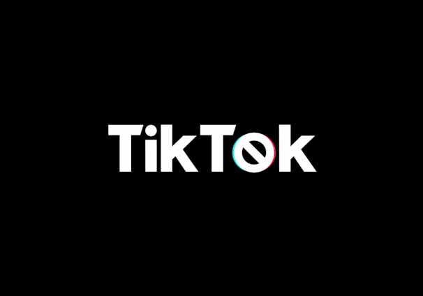 A minimalist logo featuring the word TikTok in a bold, white font centered on a black background. The 'o' in TikTok is stylized with a design resembling a musical note, incorporating subtle blue and red hues.