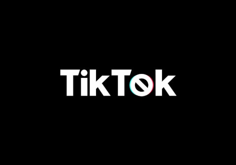A minimalist logo featuring the word TikTok in a bold, white font centered on a black background. The 'o' in TikTok is stylized with a design resembling a musical note, incorporating subtle blue and red hues.