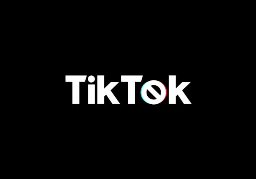 A minimalist logo featuring the word TikTok in a bold, white font centered on a black background. The 'o' in TikTok is stylized with a design resembling a musical note, incorporating subtle blue and red hues.
