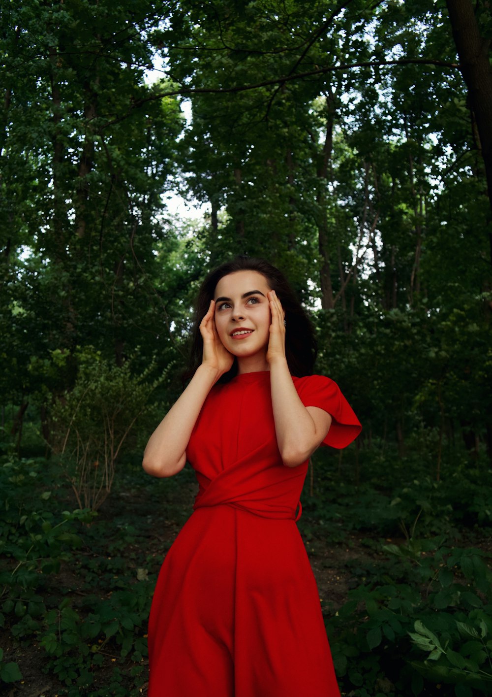 woman in red dress standing under green tree during daytime