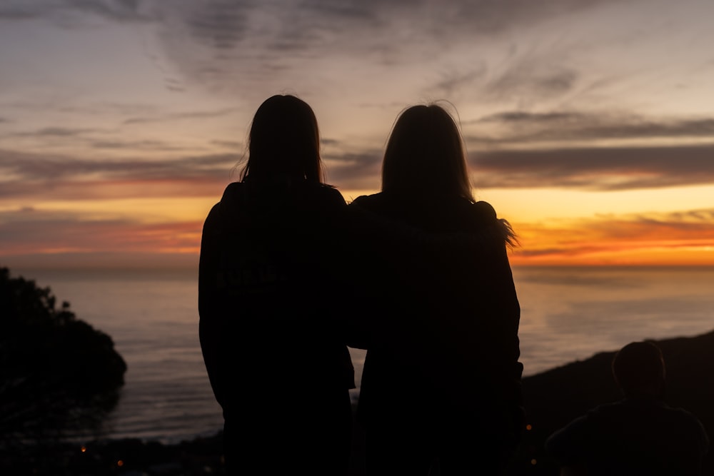 silhouette d’homme et de femme debout sur le bord de mer pendant le coucher du soleil