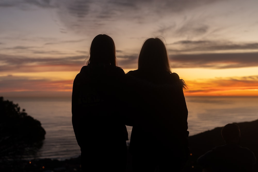 Silueta del hombre y de la mujer de pie en la orilla del mar durante la puesta del sol