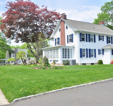 white and gray house near green grass field and trees during daytime