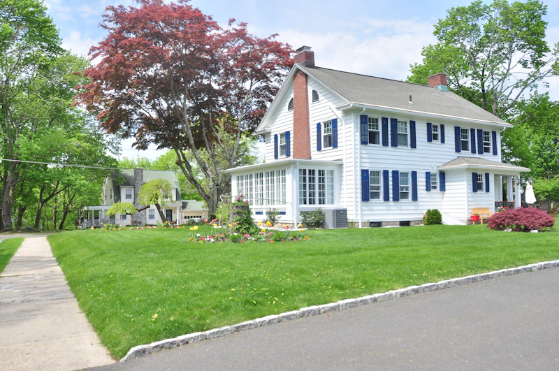 White colonial-style house with gray trim on a green lawn surrounded by trees