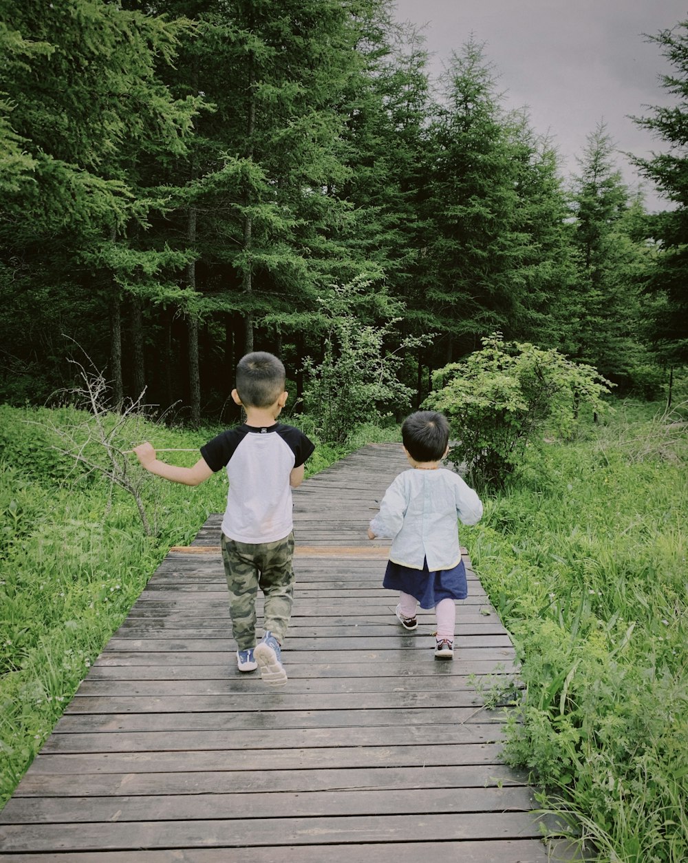 boy in white t-shirt and blue denim jeans walking on wooden pathway