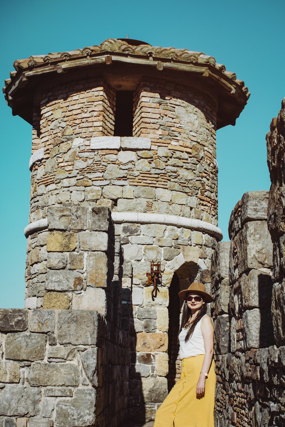 Frau im weißen Langarmhemd tagsüber auf brauner Ziegelmauer stehend