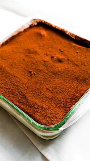 Close-up of a perfectly layered tiramisu in a delicate glass cup, dusted with cocoa powder.