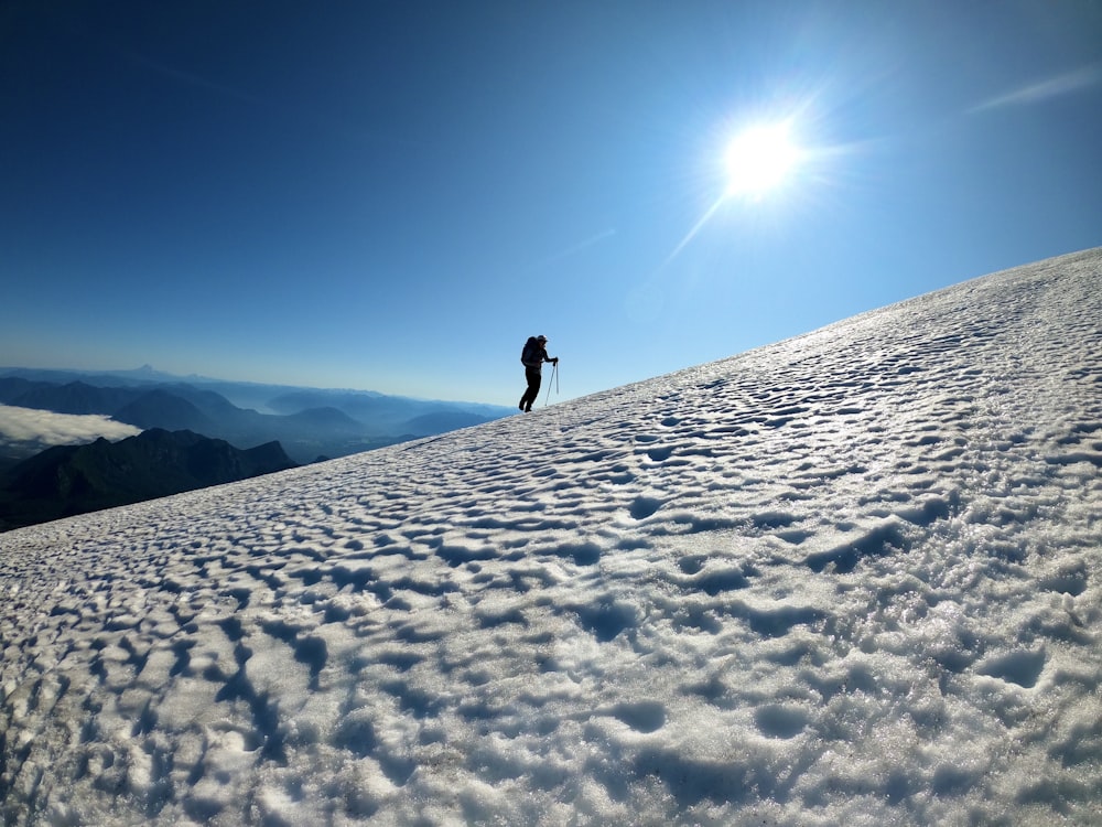 person in black jacket and black pants walking on snow covered ground under blue sky during