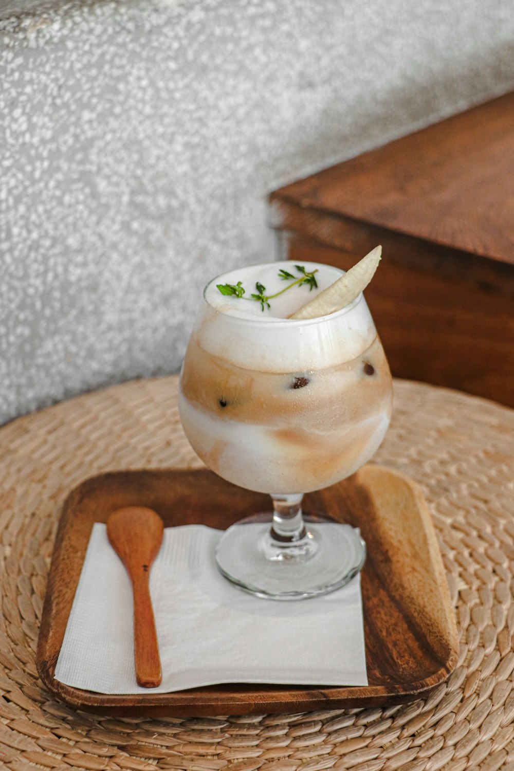 clear glass cup with white liquid and green leaf on brown wooden coaster