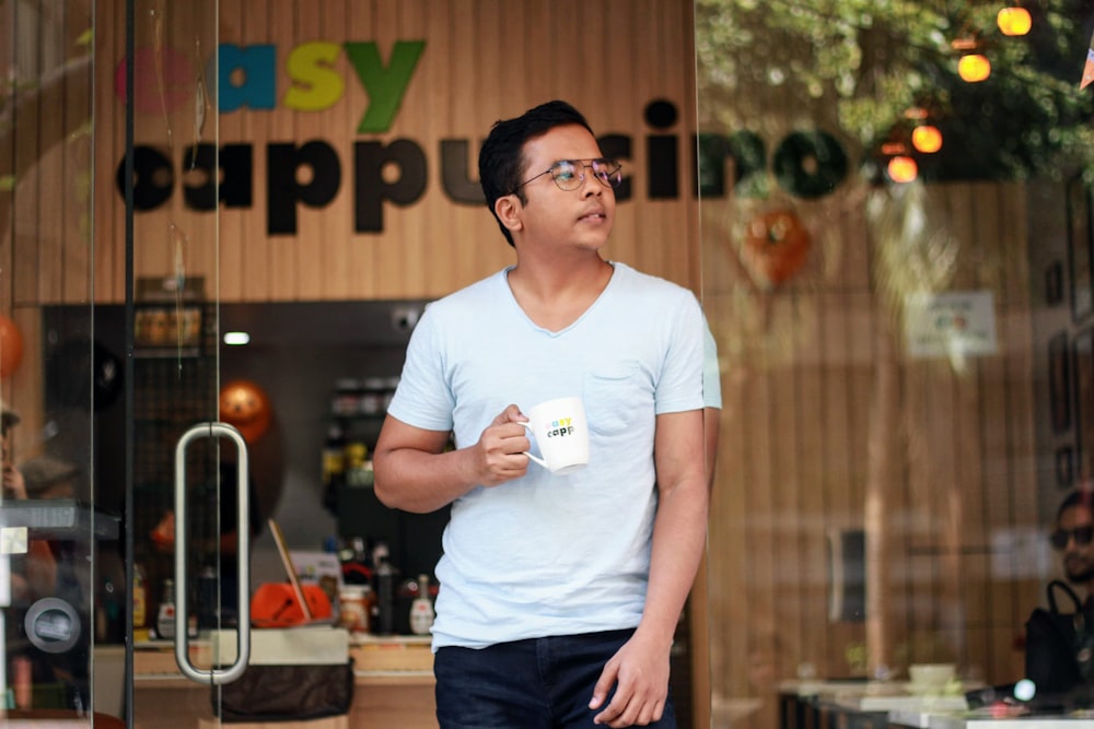 man in white crew neck t-shirt and black shorts holding white ceramic mug