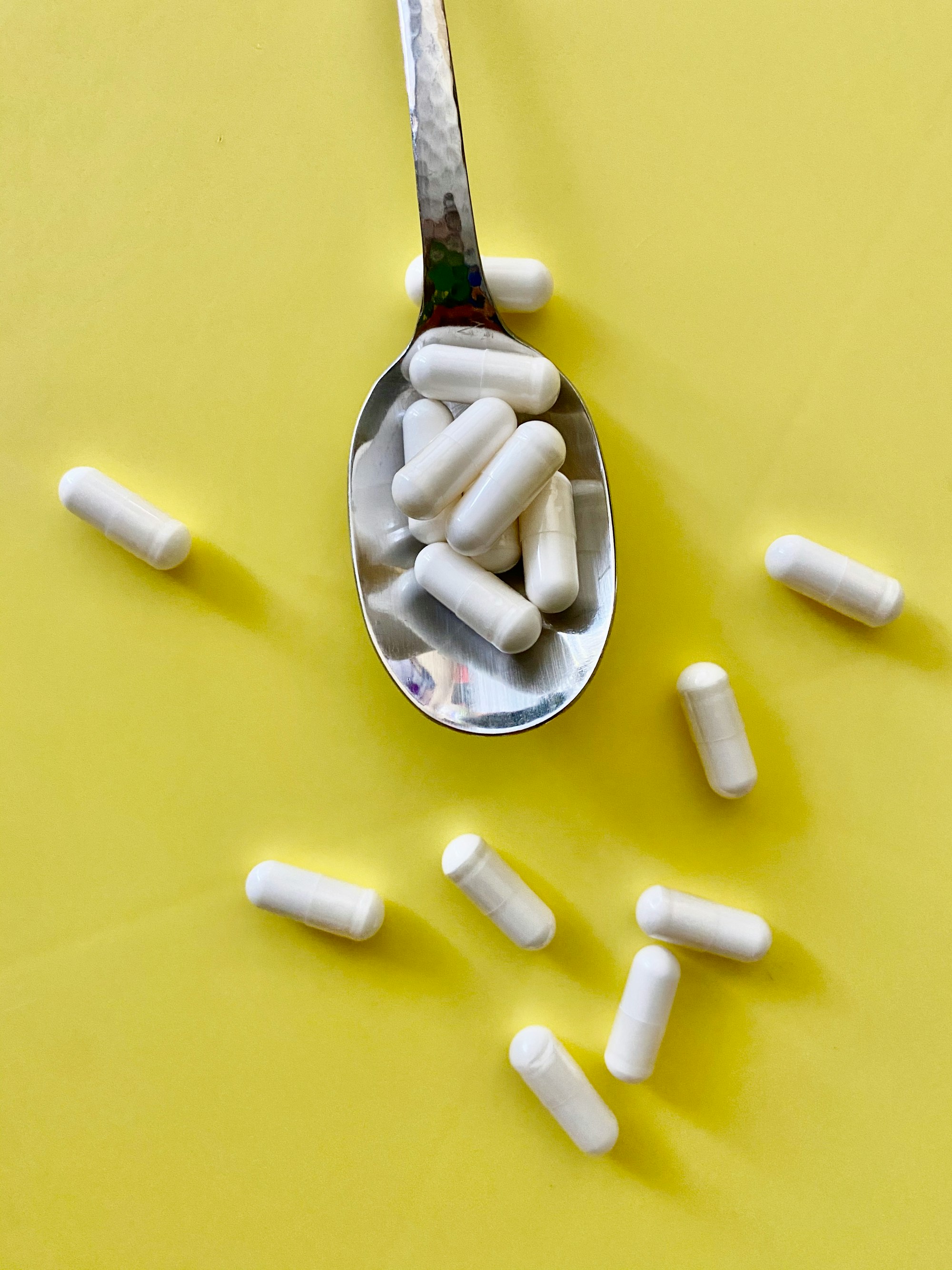 White capsules spilling out of a spoon onto a yellow table. 