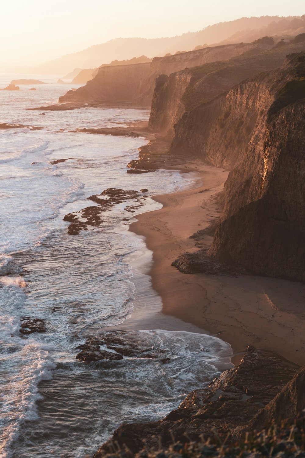 brown rocky mountain beside sea during daytime