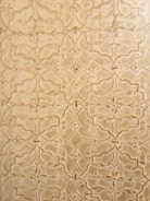 An intricate pattern of floral and geometric shapes etched into a textured surface. The design features repeating motifs with a slightly vintage and ornate appearance.
