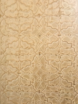 An intricate pattern of floral and geometric shapes etched into a textured surface. The design features repeating motifs with a slightly vintage and ornate appearance.