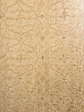 An intricate pattern of floral and geometric shapes etched into a textured surface. The design features repeating motifs with a slightly vintage and ornate appearance.