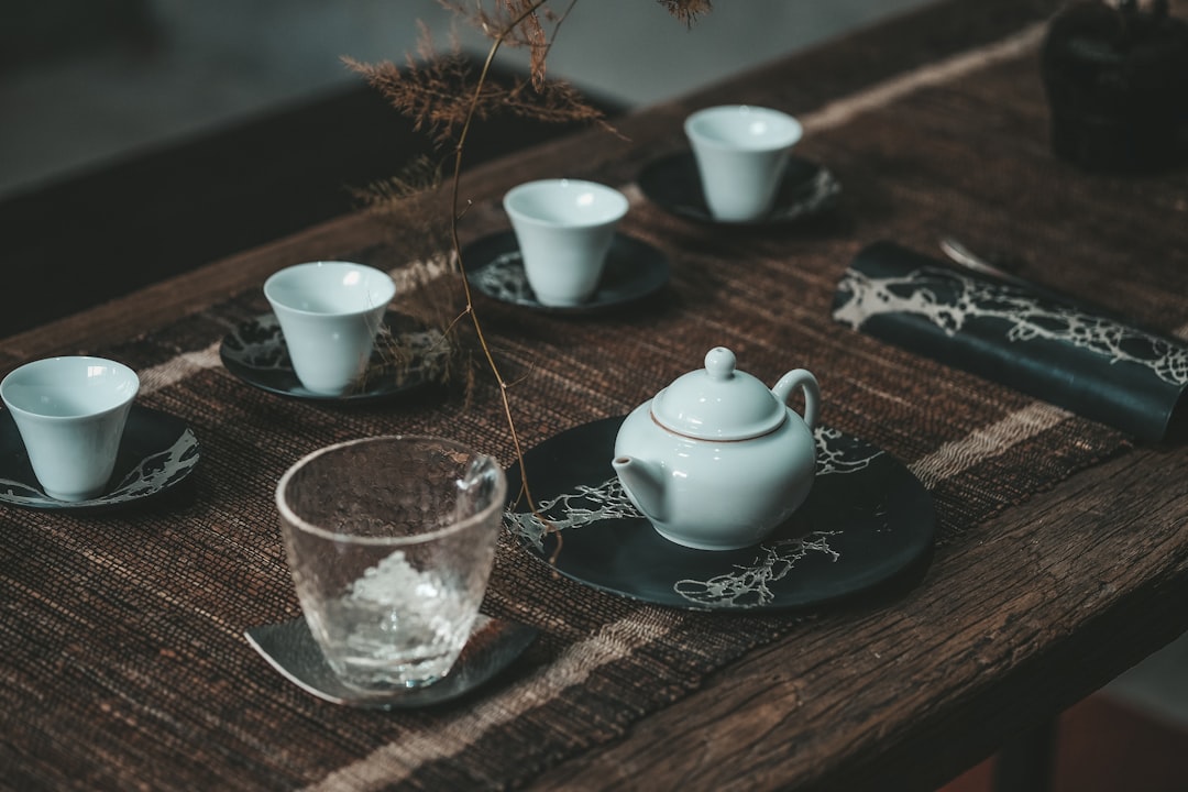 white ceramic teapot beside clear drinking glass on brown wooden table