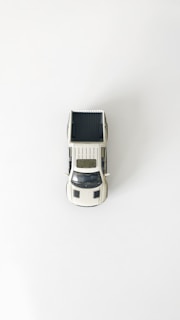 A miniature model of a white pickup truck is placed on a plain white background. The truck is viewed from a top-down perspective, highlighting its truck bed and the detailing on its roof and hood.