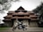 A traditional South Indian temple with intricate architectural details and terracotta-tiled roofs, set amidst a lush green environment with a classic motorcycle parked in front of it.