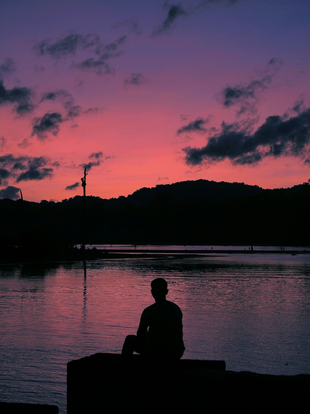 silhouette dell'uomo seduto sulla roccia vicino allo specchio d'acqua durante il tramonto