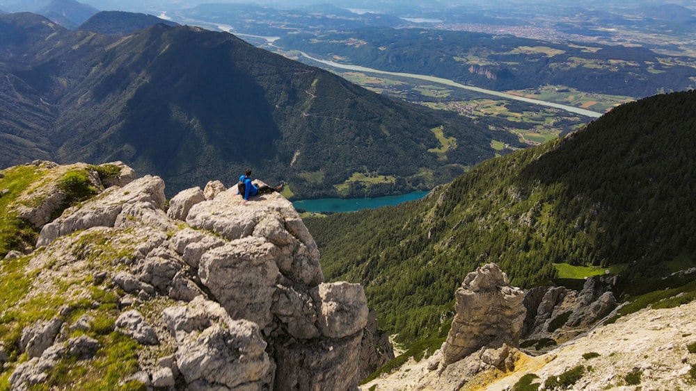 person in blue jacket sitting on rock formation during daytime