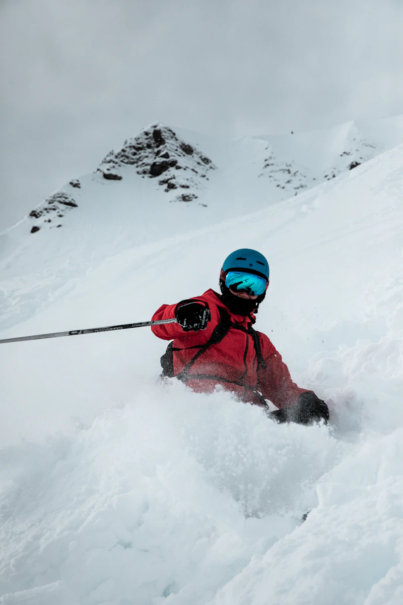 Freerider in a red jacket carving through deep powder beneath rocky peaks