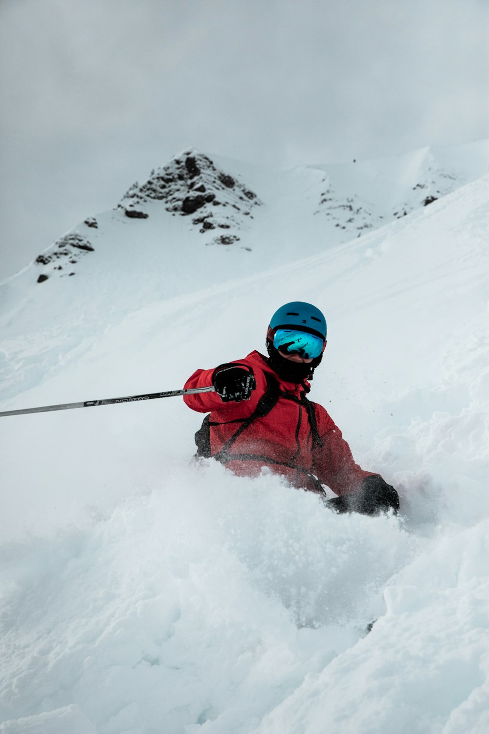 person in red jacket and black pants wearing red goggles on snow covered mountain during daytime