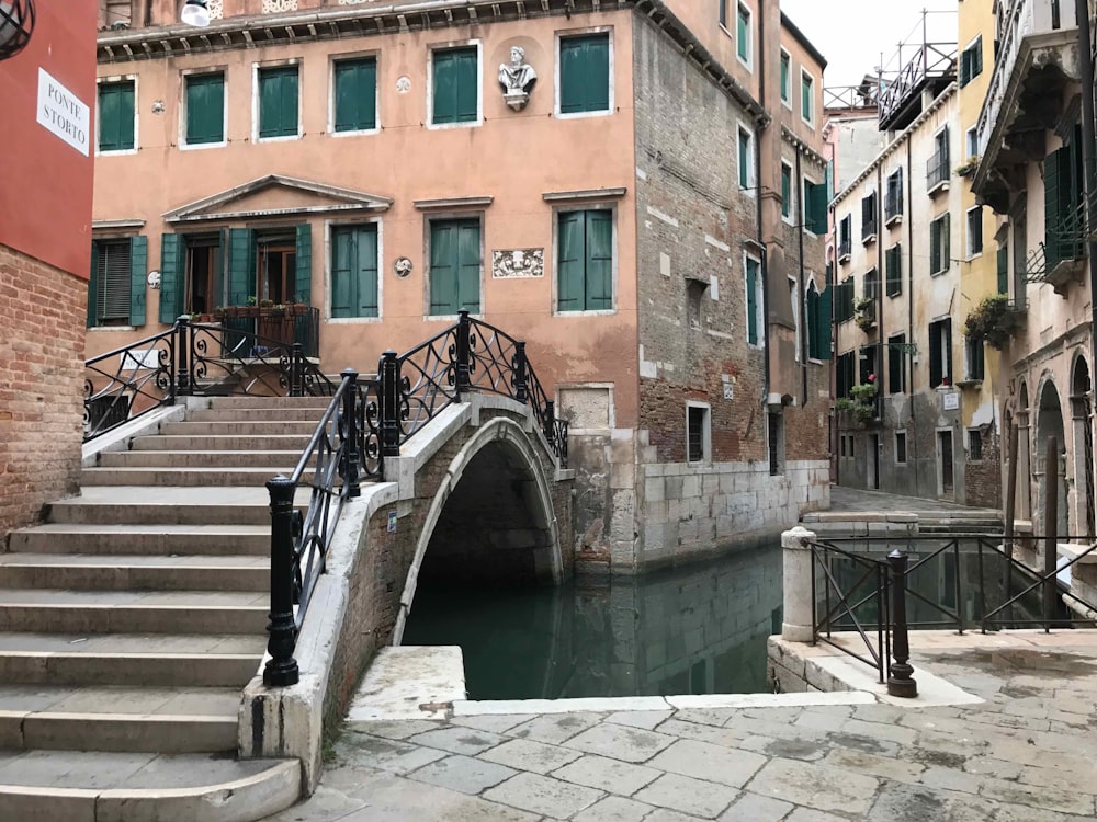 white and brown concrete bridge over river between brown concrete buildings during daytime