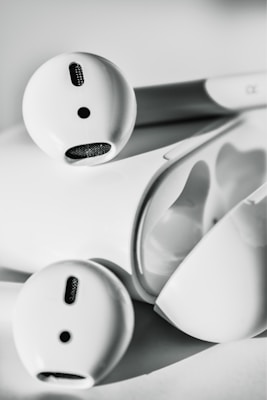 A close-up view of a pair of wireless earbuds resting on their charging case. The design is sleek and minimalist, with smooth surfaces and precise details.