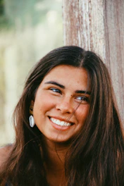 A young woman wearing layered necklaces and minimalist earrings, smiling in natural sunlight.