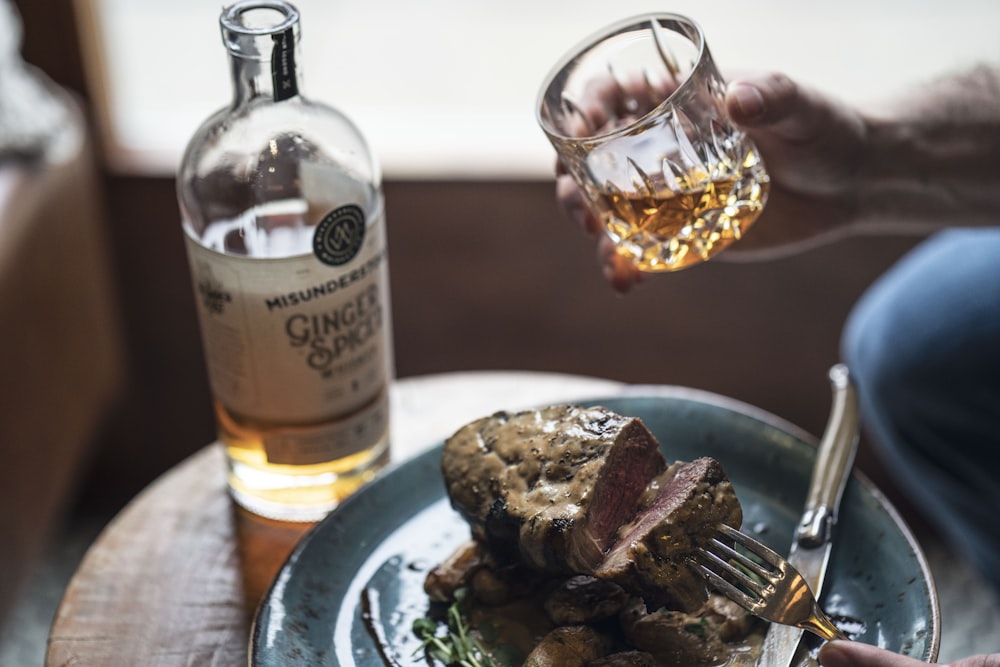 clear glass bottle beside cooked meat on white ceramic plate