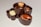 Three pieces of gourmet chocolate arranged on a light surface. Each piece is uniquely crafted with different types of nuts on top, including a hazelnut and an almond, and filled with different flavors. The chocolate is presented in a visually appealing manner with smooth textures and glossy surfaces.