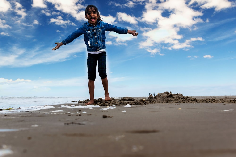 girl in blue jacket and black shorts standing on beach shore during daytime