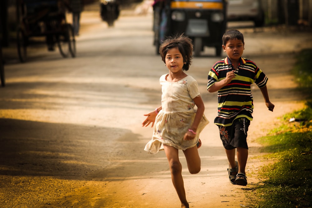 2 children running on road during daytime
