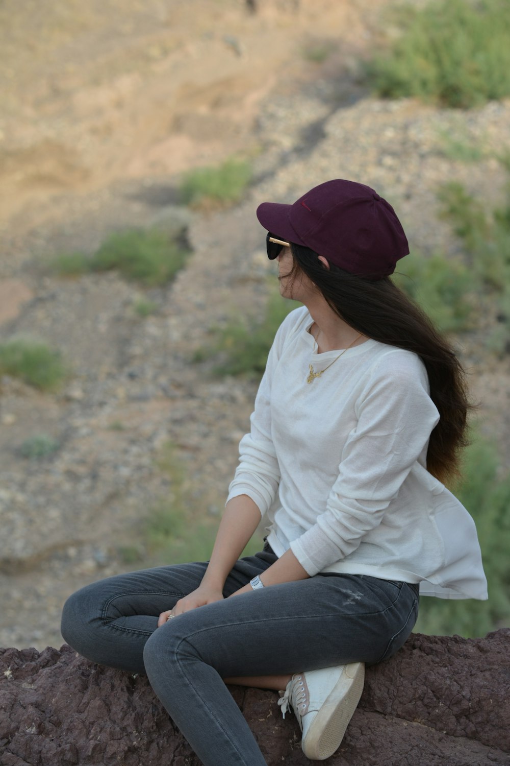 woman in white dress shirt and blue denim jeans sitting on brown rock during daytime