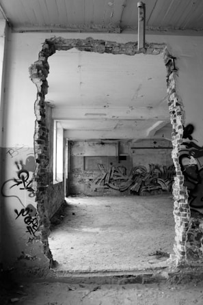 Black and white photo of an abandoned urban wall with peeling paint and graffiti.