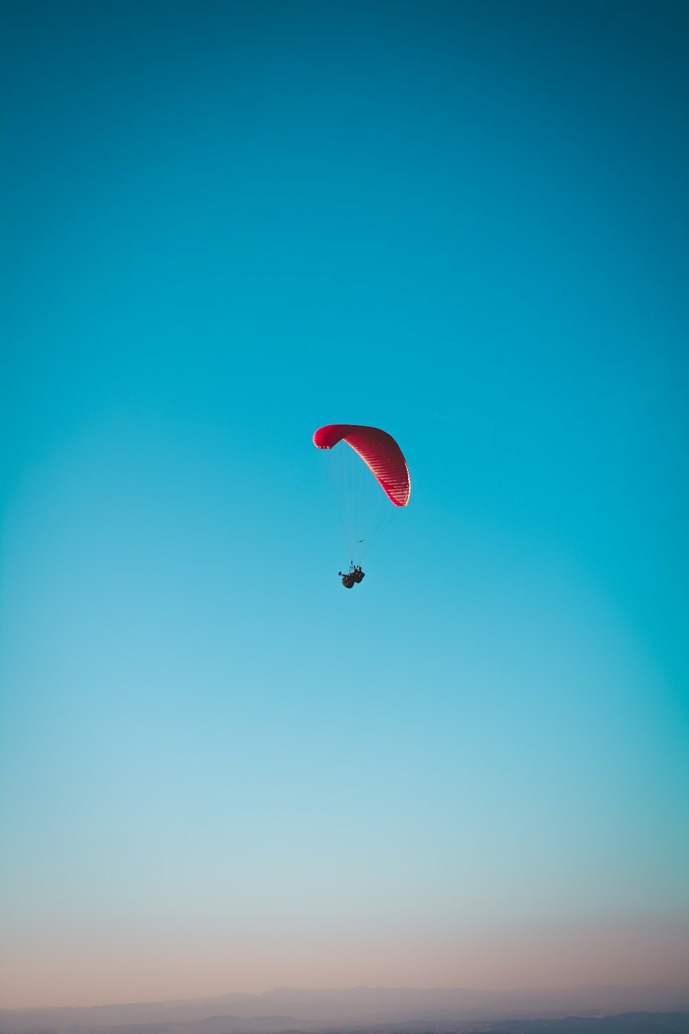 空中に浮かぶ赤いパラシュートの人