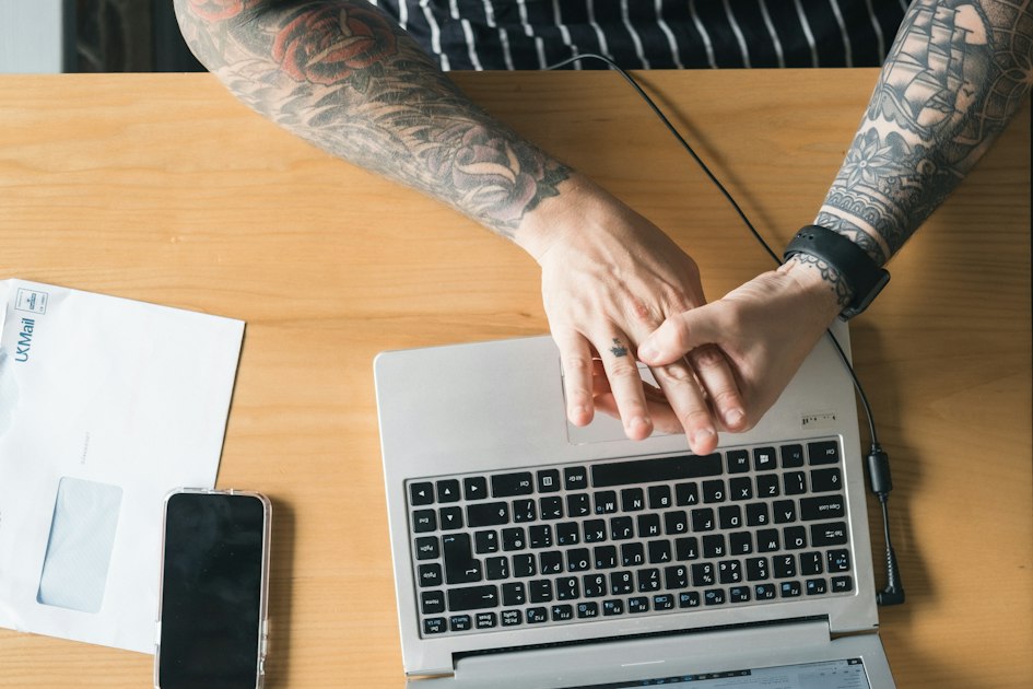 Hands resting on a laptop keyboard next to a phone and an envelope on a wooden desk.