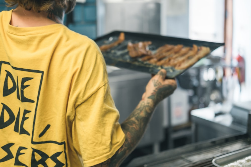 person in yellow long sleeve shirt holding brown pastry