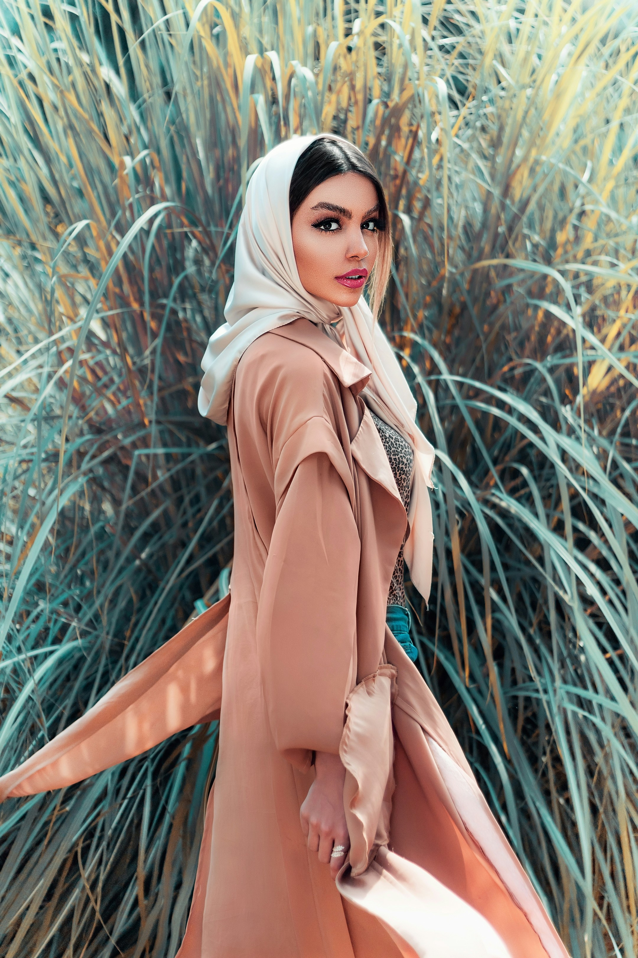 wanita berjilbab coklat berdiri di dekat tanaman hijau di siang hari