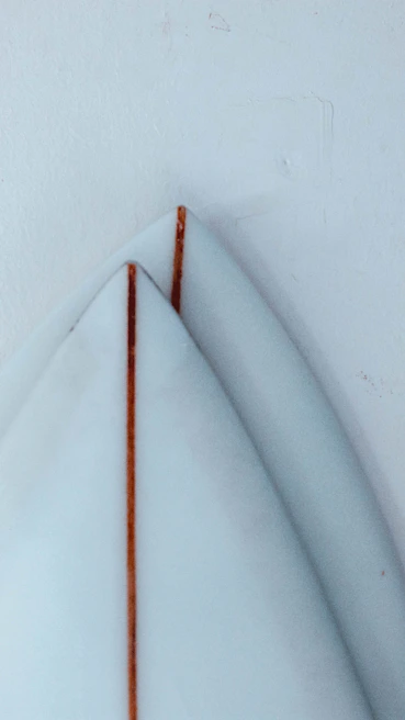 Close-up of a minimalist surfboard leaning against a wall with a folded type of pose hoodie draped over it.