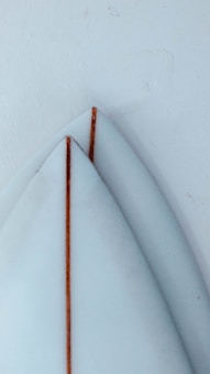 Two surfboard tails with a light blue color and wooden stringers are placed against a pale-colored wall. The boards display clean lines and minimalistic design.